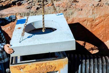 İnşaat işçisi inşaat alanındaki rögar kapağının üzerine beton kapağı dikkatlice yerleştirdi.