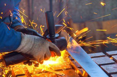 Worker skillfully operates grinding tool, creating bright sparks while shaping metal in busy metal fabrication workshop. clipart