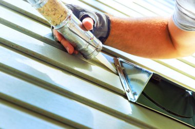 Kaliteli işçiler inşaat sırasında dışarıda caulk silah araçları kullanarak evin dışındaki metal menfezleri kapatıyor.