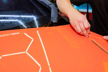 Skilled technician applies precise cuts to bright orange wrap, creating unique design on vehicle. clipart