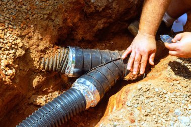 İşçi inşaat alanındaki siperlerdeki siyah plastik drenaj borularını birbirine bağlıyor ve toprak ortasındaki düzgün kurulumu sağlıyor..
