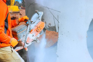 Construction worker operates concrete cutting saw, creating dust during build works area at construction site clipart