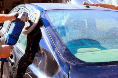 Technician worker meticulously polishes car surface using rotary buffer tools at car service shop clipart