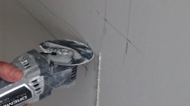 İşçi, modern bir evde yenilenmeye hazırlanmak için duvardaki düz bir hattı kesmek için elektrikli bir alet kullanıyor..