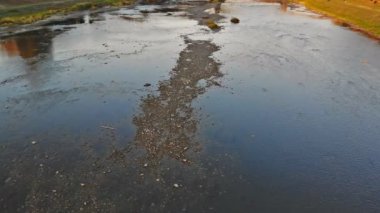 Sakin bir nehir günbatımının parlayan renklerini yansıtırken çakıl taşları barışçıl bir atmosfer izlenimi veriyor..