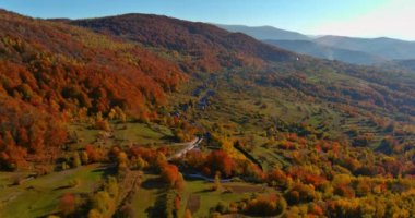 Sonbaharda huzurlu kırsal bölgede güneş parlarken tepeleri renkli sonbahar yaprakları kaplıyor..