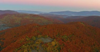 Parlak sonbahar yaprakları, güneş batarken tepeleri örtüyor ve manzaranın üzerine sıcak renkler döküyor..