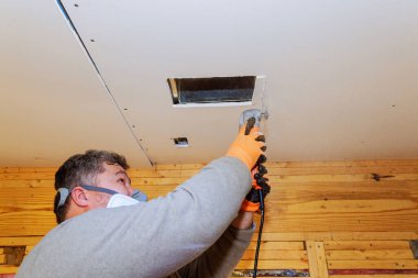 İşçi, havalandırma için alçıpan kesmek için elektrikli testereyi kullanıyor..