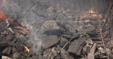 Mangal kömürü tutuşturur ve bir ızgarada duman çıkarır, canlı bir açık hava pişirme deneyimi sergiler..