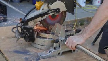 Metal bir boru kesmek için elektrikli testere kullanan bir insan, iyi aydınlatılmış bir atölyede kıvılcımlar yaratır..