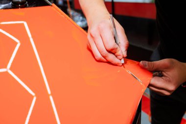 İşçi parlak turuncu madde üzerine geometrik desen çizerek, araba servis istasyonunda kesinliği vurguluyor