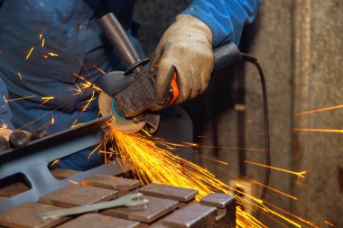 Çelik işçisi metal üzerinde öğütme aleti kullanıyor, metal üretimi sırasında atölyede parlak kıvılcımlar üretiyor