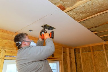 İşçi bitmemiş bir odada güç tornavidayı kullanırken dikkatlice tavana alçıpan yapıştırır.