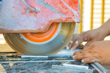 İşçi, parlak atölyedeki fayansları tam olarak şekillendirmek için kesme aracı kullanır, göreve dikkatle odaklanır.