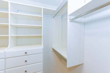 Beyaz rafların yer aldığı parlak, geniş dolap, kıyafet düzenlemek için askı, aksesuarlar..