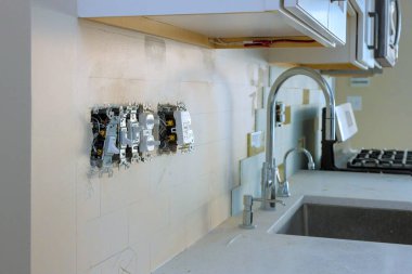 İşçiler mutfak tadilatına elektrik prizleri kuruyor, gün ortasında modern apartman tasarımı sergileniyor.