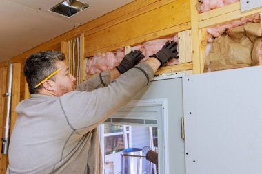 Eldiven giyen tamirci, ev tadilatı sırasında duvarlara yalıtım yapıyor.