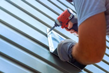 Marangoz, tornavida matkabıyla metal havalandırma kaplama panellerini koruyor.