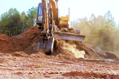 Ağır kazıcılar aktif olarak toprak taşıyorlar. İnşaat alanındaki enkazlar iş ekipmanlarıyla çevrili.