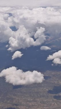 Hava görüntüsü, parlak bir gökyüzünün altında, dağların üzerinde süzülen tüylü bulutların sakin bir atmosfer yarattığını gösteriyor..