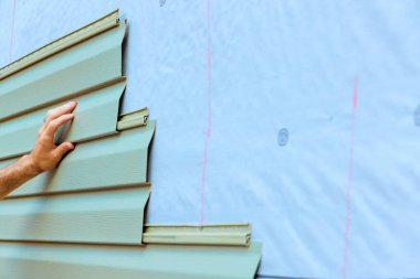 İşçi inşaat yenileme sürecinde evin dış tarafına yeni yeşil kaplama levhaları uyguluyor