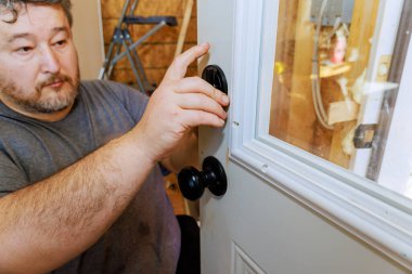 İşçi, siyah kapı tokmağını dikkatlice ahşap kapıya yerleştirir, ev işlerinde çalışır.