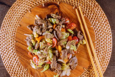 Tahta tabakta servis edilen taze sebzelerle karıştırılmış leziz kızarmış sığır eti. Yemekte paylaşmak için mükemmel..