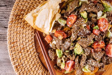 Yumuşak sığır eti, sebzelerle kızarır. Dokuma tabağında susam tohumu, yanında da kızarmış tortilla..