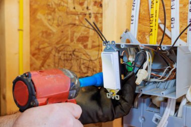 Bir elektrikçi evdeki duvar paneli kutusunun içine kablo bağlıyor..