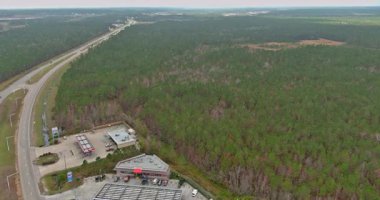 Hava görüntüsü, yoğun orman ve yakınlardaki ticari tesislerle birlikte otoyolun bir bölümünü gösteriyor..