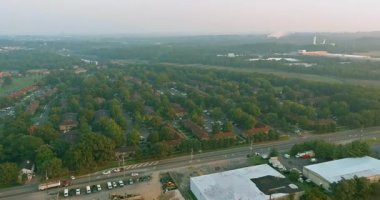 Hava perspektifi, şafak vakti ağaçlar ve sanayi binalarıyla çevrili bir banliyö mahallesini gösteriyor.