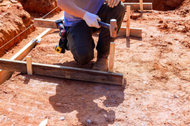 İnşaat işçisi temel düzeni kurmak için kazıkları yere çakıyor.