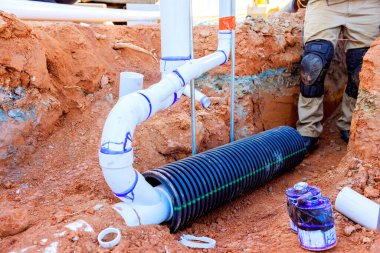 İşçiler inşaat alanındaki sipere siyah drenaj borusu yerleştirmekle meşguller.