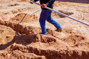 Temelde kumlu zemini şekillendirmek için elektrik boruları döşeyen bir işçi