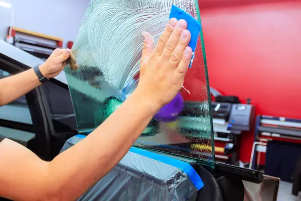 Teknisyen, iyi aydınlatılmış garaj ortamında arabanın camını temizlemek için mavi sünger kullanıyor..