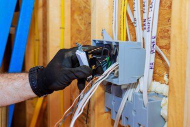 Bir elektrikçi, elektrik kablolarını evdeki bağlantı kutusuna bağlayıp güvenlik önceliğini belirliyor.
