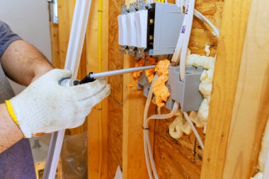 Bir elektrikçi, yeni ev inşa edilirken boşlukları köpük yalıtımıyla kapatırken elektrik prizleri kuruyor.