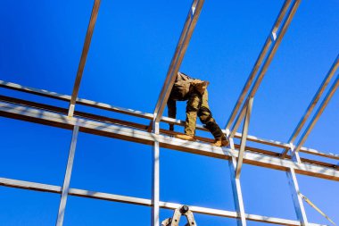 İnşaat işçisi çelik iskeletin üstüne yerleştirilmiş, dikkatlice metal kirişler yerleştiriliyor.