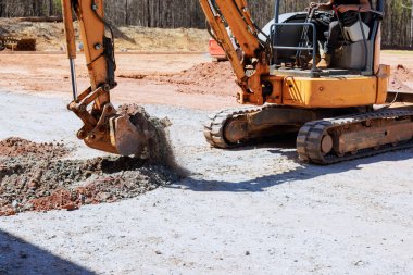 Ağır makineler iş başında, çukur kazmak için kazıcı kullanırken inşaat alanında çakıl taşları hareket ediyor