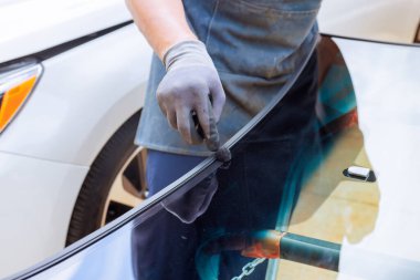 Teknisyen, araba tamirhanesinde reçine ile tamir edilen arabanın ön camını yapıştırıyor.