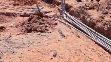 Temelde kumlu zemini şekillendirmek için elektrik boruları döşeyen bir işçi