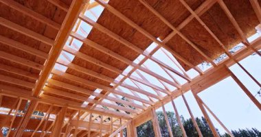 Bina inşaatı sırasında ahşap çatı kirişleri ve çerçeve, yapısal iskeleti, oryantasyon iplikçikleriyle ve arka planda görünen ağaçlarla korunmasız ahşap kirişlerle gösteriyor.