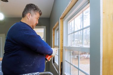 İşçi, evin içini yenilerken pencerelere yalıtım dolgu köpüğü sürüyor.