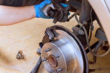 Tamirci, iyi aydınlatılmış garajda çalışırken arabanın fren kalibresini değiştiriyor..