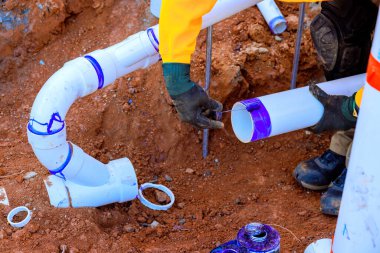 İnşaat işçileri siperlerde PVC borularını birleştiriyor, atık su tesisatı için güvenli bağlantı sağlıyorlar..