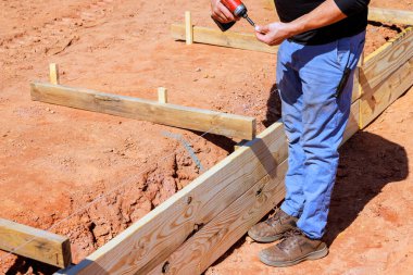 İnşaat işçisi, inşaat sahasında çalışma gününde ahşap formları güvence altına almak için matkap kullanıyor.