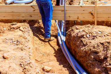 İnşaat işçisi, elektrik pvc borularını dökerken temel siperin üzerine tahta kirişler yerleştiriyor.