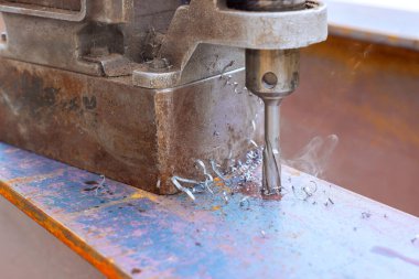 Matkap metal kirişleri deliyor, yoğun atölyede talaş dumanı çıkarıyor.