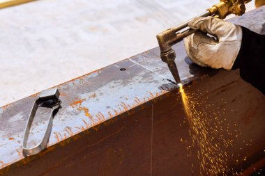 İşçi ustalıkla kaynak meşalesi kullanarak metal kirişi kesip inşaat alanında kıvılcımlar üretiyor..