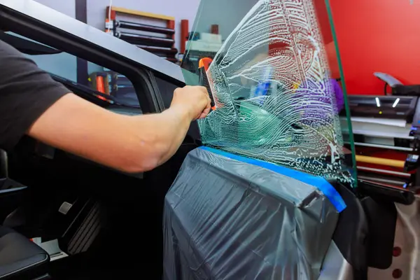 Teknisyen, atölyede kesin olarak temiz kurulum sağlarken arabanın kapısına renkli film uygular.